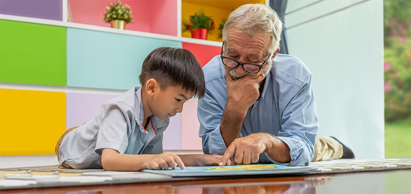 An elderly man reading with a preschool age boy.